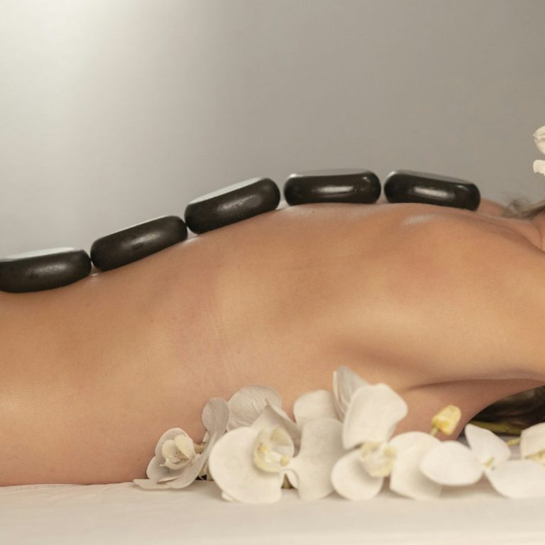 A person lying on their stomach with smooth stones and flowers on their back.